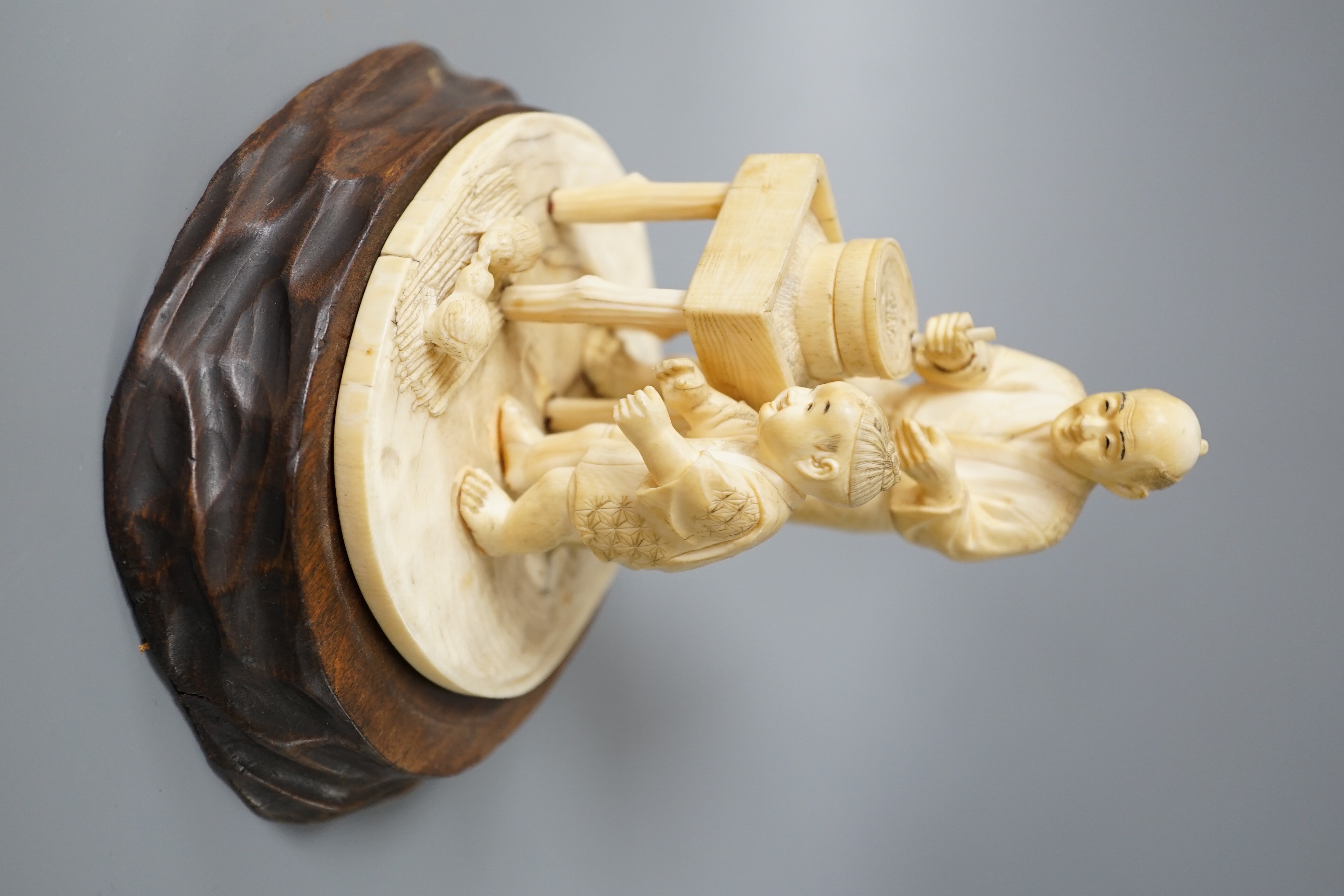 A Japanese ivory okimono of man and boy at a grindstone, Meiji period, signed, wood stand. 15cm total height